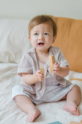 Smiling baby model wearing the ivory Lucent Short Sleeve Cardigan. Comfortable baby cardigan, perfect summer outfit for infants.